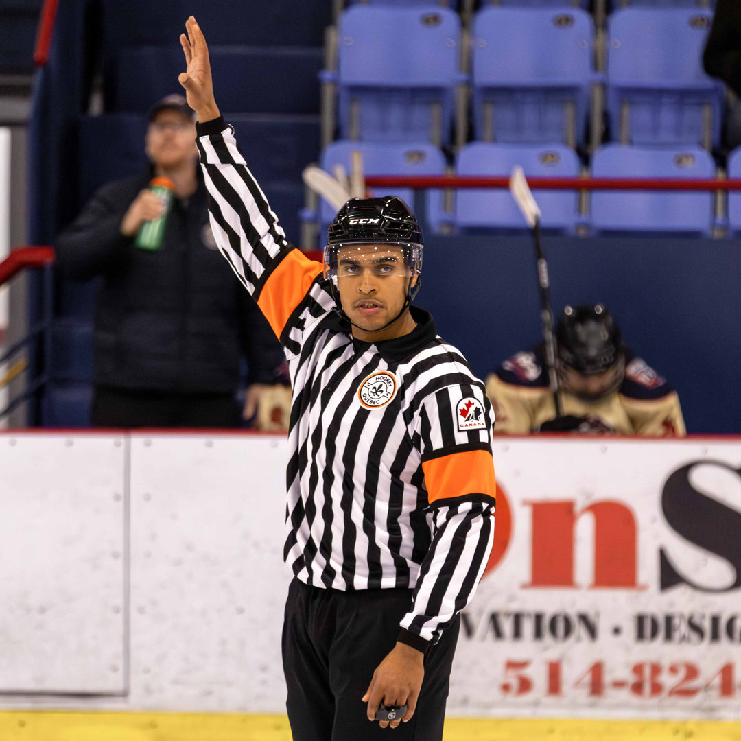 Referee in a striped jerse with orange arm bands on an ice hockey rink